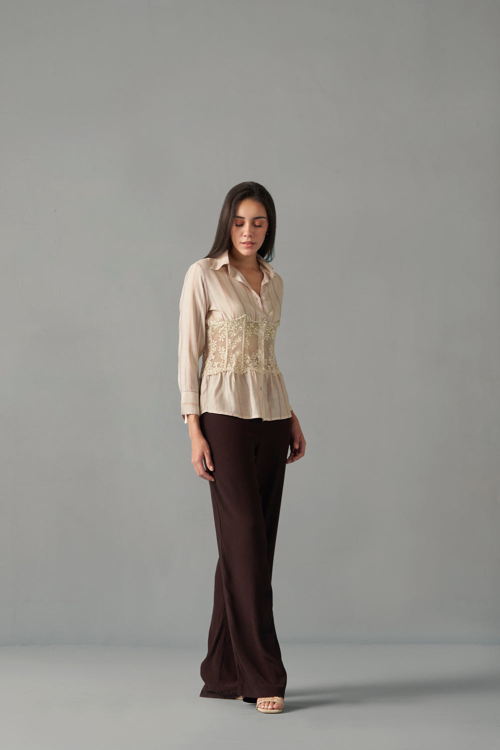 Women's embroidered corset detail shirt with striped pattern , Woman wearing a beige blouse and brown pants against a gray background