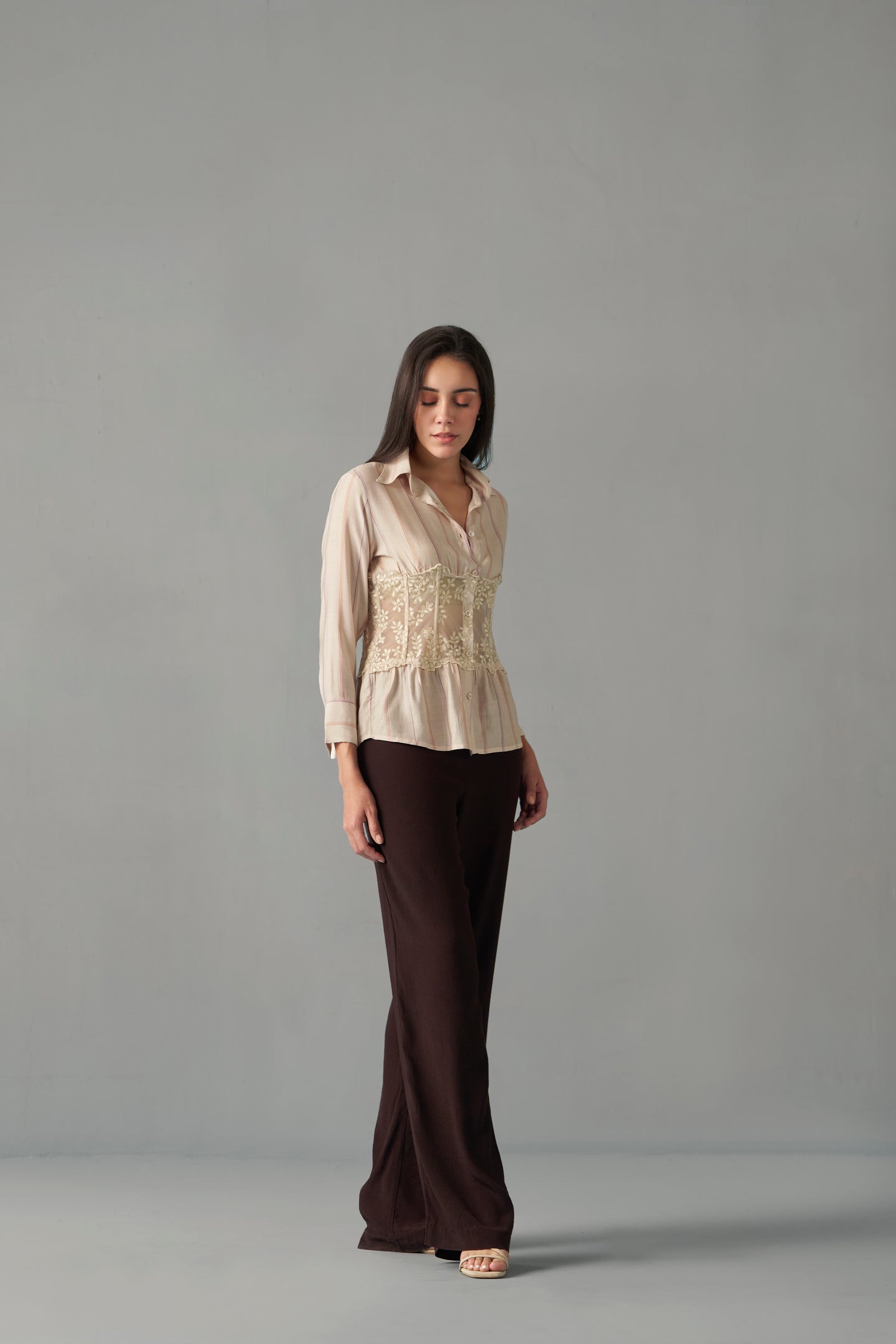 Women's embroidered corset detail shirt with striped pattern , Woman wearing a beige blouse and brown pants against a gray background